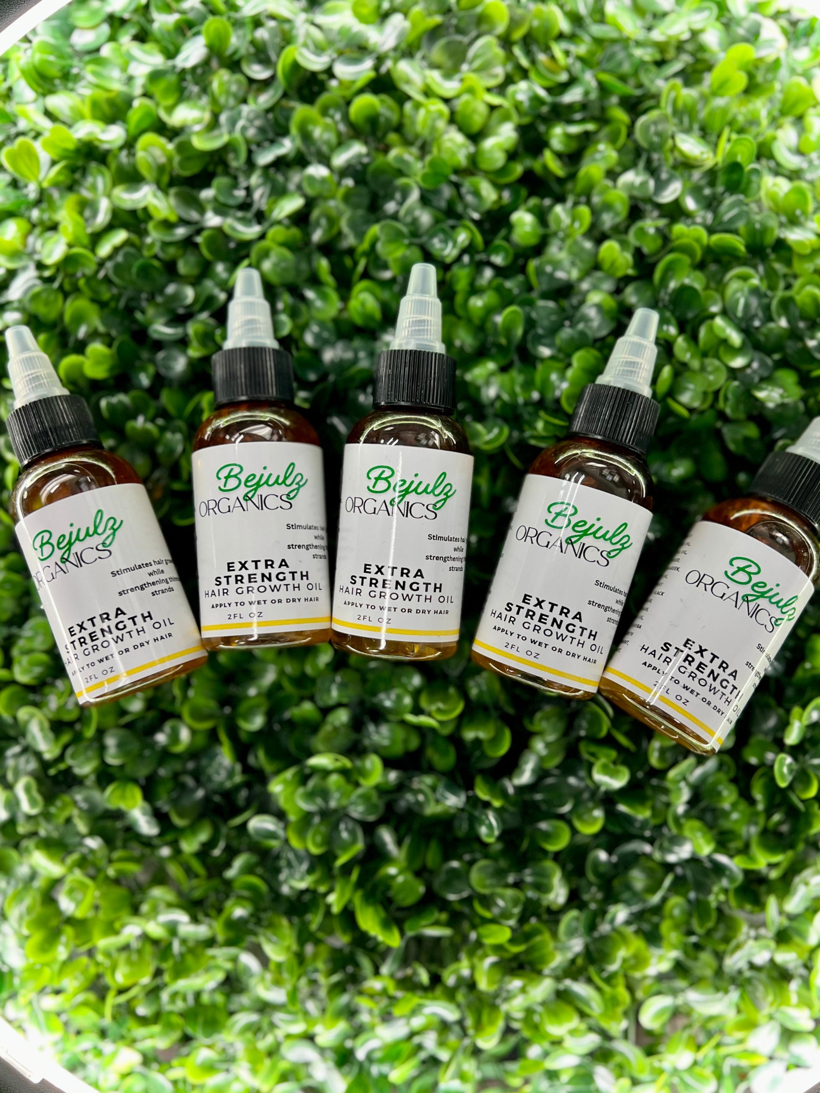 Three bottles of Bejulz Organics Extra Strength Hair Growth Oil on a green leafy surface.